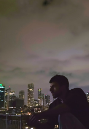 Klimatyczne, nocne ujęcie z filmu. Dwie ciemne sylwetki na pierwszym planie na dachu, zwrócone do siebie. Tło to błyszcząca panorama metropolii pod dramatycznym, zachmurzonym niebem.