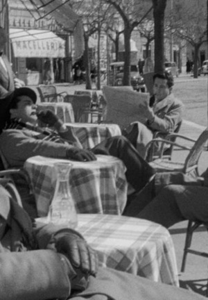 [Czarno-biały kadr z filmu. Czterech mężczyzn siedzi przy stolikach restauracyjnych.]