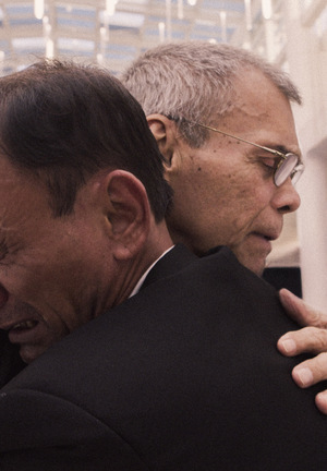 Kolorowe zdjęcie. Zbliżenie, dwóch dorosłych mężczyzn przytula się do siebie, widzimy ich twarze na ramionach. Oboje płaczą.