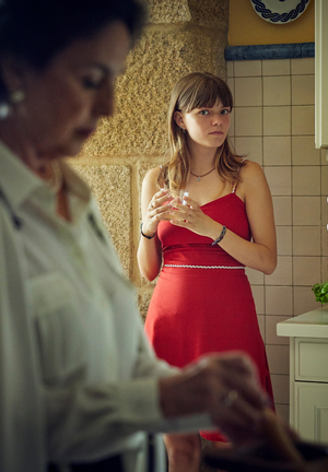 Kolorowe zdjęcie. Nastolatka w czerwonej sukience stoi w kuchni i przygląda się kobiecie krojącej sałatkę.