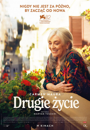„Plakat filmu „Drugie życie”. Uśmiechnięta starsza kobieta o siwych włosach opiera się o balkon wśród czerwonych kwiatów. U góry hasło: „Nigdy nie jest za późno, by zacząć od nowa”. Na dole tytuł filmu i nazwiska twórców.”