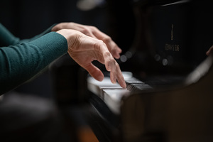 Dłonie pianisty uniesione nad klawiaturą fortepianu.
