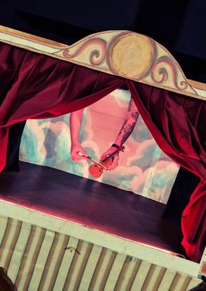 Grafika reklamowa Gdy Opera drzwi otwiera. Scena z rozpostartymi kotarami. Ręce aktorki trzymają małe skrzypce i smyczek.