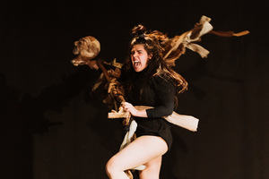 kadr z przedstawienia, skacząca kobieta, krzycząca, która trzyma w rękach kij ze szmacianą głową.