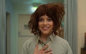 Kadr z filmu &amp;amp;amp;amp;quot;KLARA I SŁOŃCE&amp;amp;amp;amp;quot;. Aktorka Jenna Ortega jako Klara, Sztuczna Przyjaciółka, siedzi przy stole w przeszklonym pomieszczeniu. Patrzy w obiektyw, a w tle widać rozmazaną postać innej osoby.