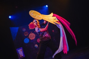 Zdjęcie ze spektaklu. Aktorka w kolorowym kostiumie animuje lalkę planety/planszetę.