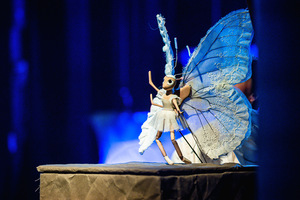 Grafika przedstawia lalkę motyla w kolorze białym, animowaną przez aktorkę.