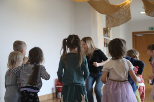 Grupa dzieci razem z prowadzącą tańczą w jasnej sali.