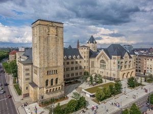 Zdjęcie gmachu budynku. Z wieżą zegarową na pierwszym planie. Widoczny dziedziniec przed zamkiem oraz główne wejściem do zamku po prawo.