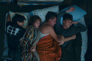[Kolorowy kadr z filmu. Czworo przyjaciół śpi razem na łóżku]