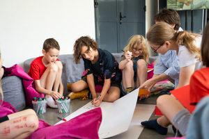 Zdjęcie przedstawia grupę dzieci siedzącą na podłodze i piszącą na dużej kartce.