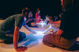 Dzieci i dorośli siedzą na podłodze mają w rękach światełka