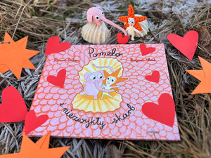 Okładka książki dla dzieci. Książka leży na trawie. Obok leżą papierowe serduszka.