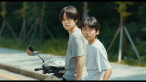 Kadr z filmu. Dwóch chłopców siedzących na skuterze.