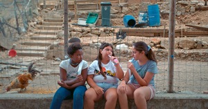 Kadr z filmu. Trzy dziewczyny siedzą na murku.