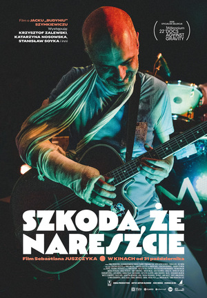 W centrum plakatu łysy mężczyzna z zabandażowaną ręką grający na gitarze. Na dole biały napis z tytułem filmu.