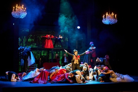 Na scenie stoi książę w eleganckim stroju. Wokół postaci księcia, na podłodze wiele leżących postaci w strojach balowych.