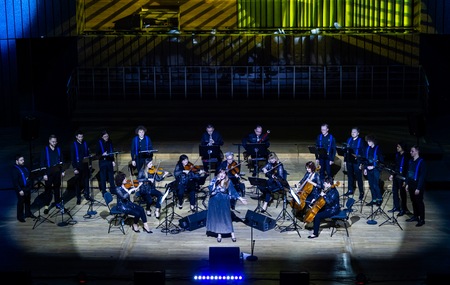 Na estradzie siedzi sześć pań, trzech panów to zespół No-Net. Za nimi stoi męski chór ubrany w czarne spodnie i koszule.Z przodu estrady w niebieskiej sukni solistka. Tło estrady w odcieniach niebieskich i złotych. Zdj. archiwum FŁ, fot. D. Kulesza