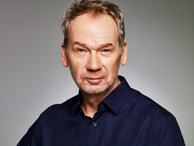 Kolorowy portret uśmiechniętego mężczyzny w ciemnej koszuli.