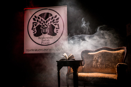 Grafika reklamowa: kremowa sofa spowita dymem, na stoliku przed nią otwarta książka, w tle logo i nazwa wydarzenia