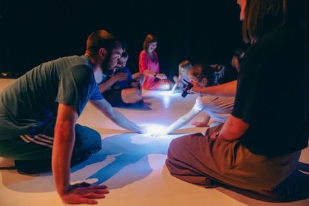 Dzieci i dorośli siedzą na podłodze mają w rękach światełka