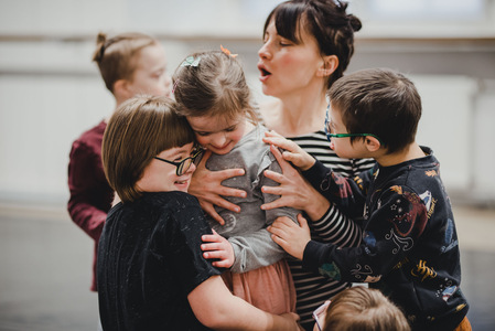 grupa osób, dzieci i dorosłych, siedzi na ziemi i się przytula