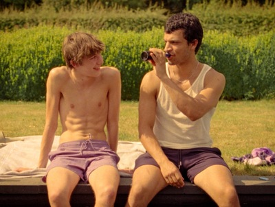 Kadr z filmu. Dwóch młodych mężczyzn siedzi na pomoście. Jest ciepło.