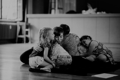 grupa osób, dzieci i dorosłych, siedzi na ziemi i się przytula