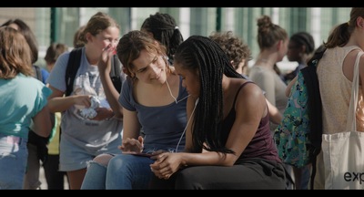 Kadr z filmu. Dwie dziewczyny siedzą na ławce i rozmawiają ze sobą.