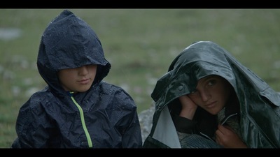 Kadr z filmu. Dwoje dzieci ubranych w peleryny przeciwdeszczowe.