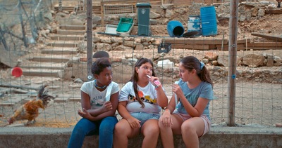 Kadr z filmu. Trzy dziewczyny siedzą na murku.