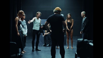 Kadr z filmu. Grupa ludzi stoi w kole w ciemnym pomieszczeniu.