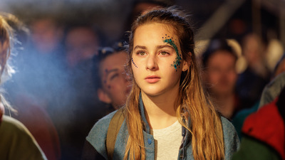 Kadr z filmu. Dziewczyna wśród tłumu. Dziewczyna ma brokat na twarzy.