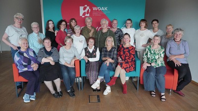 Na zdjęciu widać grupę kobiet z Zespołu Rękodzieła Artystycznego Klub Supełek. Uśmiechają się do zdjęcia. Niektóre siedzą z przodu na kanapie, a inne stoją za nimi.