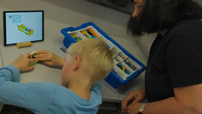 dziecko i kobieta bawią się zabawkami, robotem, stoi tablet