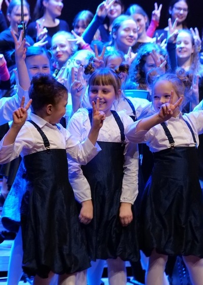 Dziewczynki z grupy najmłodszych Skowronków, uśmiechnięte, stoją na scenie podczas koncertu w sali zamkowej. Ubrane są w granatowe spódniczki i białe bluzki.